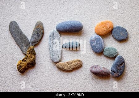Das Wort „Ja“, das mit farbigen Steinen auf weißem Sand geschrieben wurde Stockfoto