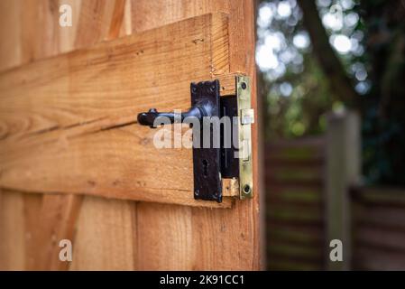 Nahaufnahme des Türgriffs aus schwarzem Metall mit Einsteckschloss an der offenen Tür des Holzschuppens im Wohngarten. Stockfoto