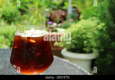 Ein Glas Eiskaffee mit verschwommenem grünem Laub im Hintergrund Stockfoto