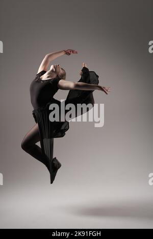 Ballerina tanzt mit Seidenstoff, moderner Balletttänzer in flatterndem, winkenden Tuch, grauer Hintergrund Stockfoto