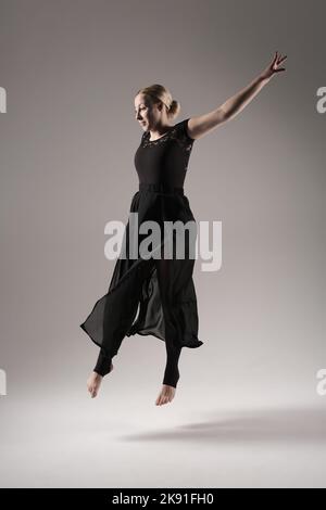 Ballerina tanzt mit Seidenstoff, moderner Balletttänzer in flatterndem, winkenden Tuch, grauer Hintergrund Stockfoto