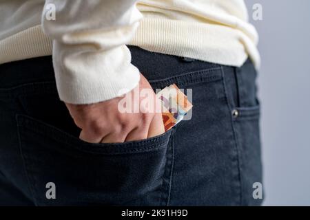 Mann, der verschiedene Euro-Banknoten in einer schwarzen Hosentasche hält Stockfoto