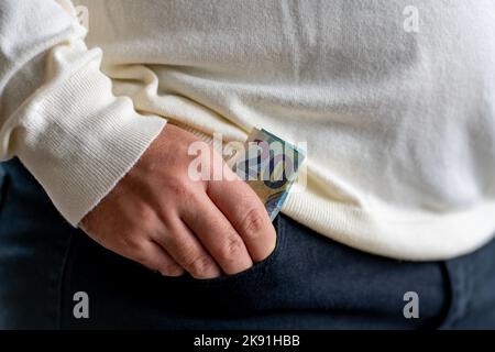 Mann hält eine 20-Euro-Banknote in der vorderen Tasche mit schwarzen Hosen Stockfoto