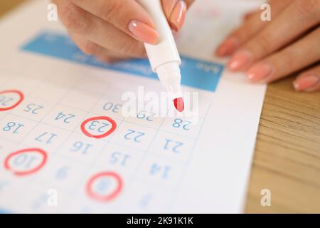 Weibliche Hand markiert Daten in Kalender mit rotem Marker Stockfoto