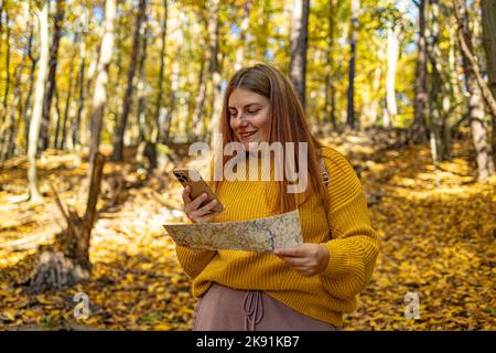 Attraktive Wanderer Mädchen zu Fuß entlang Waldweg in den Bergen und mit dem Smartphone, wegschauen. Wanderfrau in rotem Regenmantel navigiert auf dem Smartphone Stockfoto