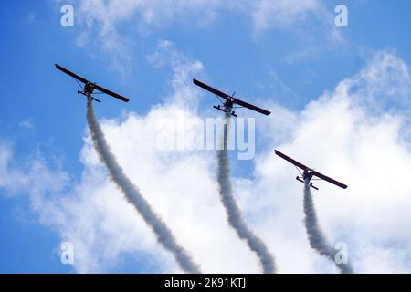 Liepaja, Lettland - 7. August 2022: Drei rote Sportflugzeuge mit Rauchstreifen machen während der Baltic International Airshow einen Gruppenflug Stockfoto