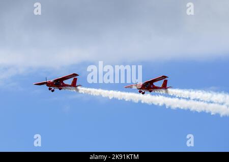 Liepaja, Lettland - 7. August 2022: Zwei rote Sportflugzeuge mit Rauchstreifen machen während der Baltic International Airshow einen Aerobatic-Gruppenflug Stockfoto