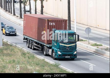 Grüner Mercedes Actros LKW, der einen roten Containeranhänger entlang der Ronda Litoral in Barcelona verladen hat Stockfoto