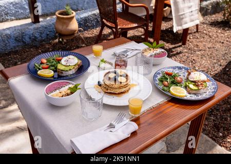 Ein guter Brunch mit Pfannkuchen und Avocado-Toast auf einem Holztisch mit Stühlen im Hintergrund. Stockfoto