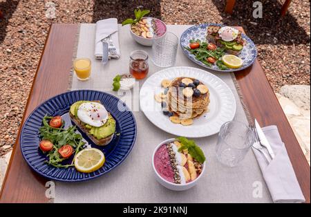 Ein leckerer Brunch mit Pfannkuchen und Avocado-Toast auf einem Holztisch. Stockfoto