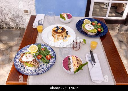 Ein guter Brunch mit Pfannkuchen und Avocado-Toast auf einem Holztisch mit einer Wand und einem Fenster im Hintergrund. Stockfoto