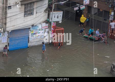 Rikscha-Besitzer kämpfen nach heftigen Regenfällen, die für Fußgänger und Pendler viel Leid verursachen, um durch eine wasserdurchflutete Straße zu waten. Der Zyklon Sitrang trifft Bangladesch, schnappt Kommunikations- und Stromverbindungen und überschwemmt Straßen, wodurch die Aktivitäten stillstehen. Stockfoto