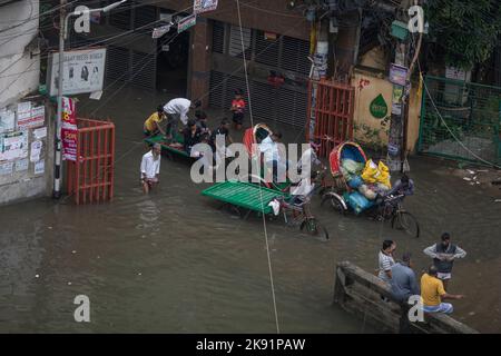 Rikscha-Besitzer kämpfen nach heftigen Regenfällen, die für Fußgänger und Pendler viel Leid verursachen, um durch eine wasserdurchflutete Straße zu waten. Der Zyklon Sitrang trifft Bangladesch, schnappt Kommunikations- und Stromverbindungen und überschwemmt Straßen, wodurch die Aktivitäten stillstehen. Stockfoto