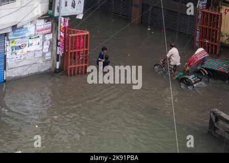 Rikscha-Besitzer kämpfen nach heftigen Regenfällen, die für Fußgänger und Pendler viel Leid verursachen, um durch eine wasserdurchflutete Straße zu waten. Der Zyklon Sitrang trifft Bangladesch, schnappt Kommunikations- und Stromverbindungen und überschwemmt Straßen, wodurch die Aktivitäten stillstehen. Stockfoto