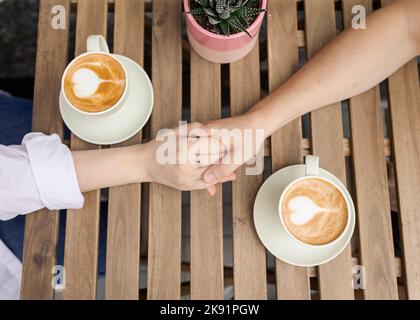 Beschnittenes Bild Paar Hände halten und Kaffeetassen Nahaufnahme außerhalb oben Stockfoto