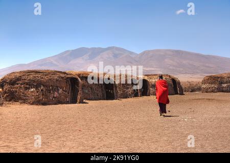 Massai Hütten mit einer Frau in rot in der Rückansicht Stockfoto