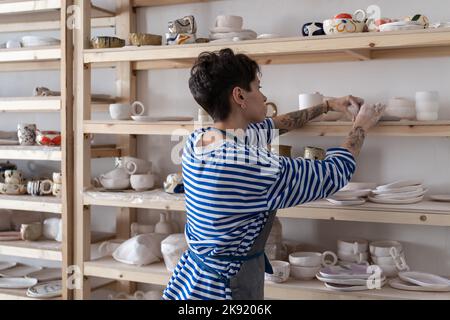 Pottery artist placing clay objects on shelves to dry before firing while working in art studio Stockfoto