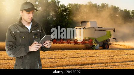 Ein Landwirt mit digitalem Tablet steuert einen autonomen Harvester auf einer intelligenten Farm Stockfoto