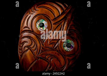 Maori Hei Tiki aus Holz, handgeschnitzt mit Paua-Muschelaugen. Neuseeländische Taonga. Nahaufnahme dunkler Hintergrund. Stockfoto