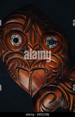 Maori Hei Tiki aus Holz, handgeschnitzt mit Paua-Muschelaugen. Neuseeländische Taonga. Nahaufnahme dunkler Hintergrund. Stockfoto