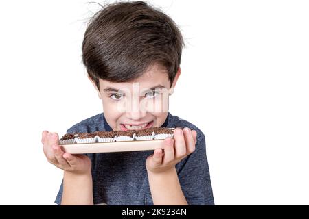 Der 9-jährige Junge zeigt seine Zähne und hält ein Tablett mit mehreren brasilianischen Fudge-Bällen. Stockfoto