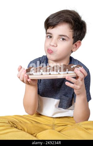 Das 9-jährige Kind hält ein Tablett mit mehreren brasilianischen Fudge-Bällen und puckert ihre Lippen. Stockfoto