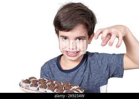 9-Jähriger hält ein Tablett mit mehreren brasilianischen Fudge-Kugeln, bereit, sie zu fangen. Stockfoto