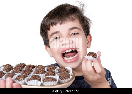 Der 9-jährige Brasilianer hält ein Tablett mit mehreren brasilianischen Fudge-Bällen und mit offenem Mund. Stockfoto