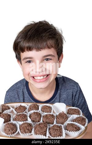 9-jähriges Kind, das ein Tablett mit mehreren brasilianischen Fudge-Bällen und einem großen Lächeln in der Hand hält. Stockfoto