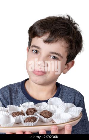 9-jähriges Kind, das ein Tablett mit brasilianischen Fudge-Bällen hält und ein zweifelhaftes Gesicht macht. Stockfoto