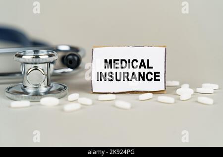 Medizinisches Konzept. Auf grauem Hintergrund ein Stethoskop, Pillen und eine Papptafel mit der Aufschrift - Krankenversicherung Stockfoto