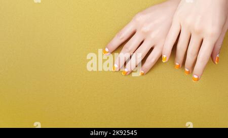 Schöne weibliche Hände mit leuchtend orange Maniküre wie Candy Corn auf gelbem Hintergrund. Gepflegte Nägel mit kreativem gelpoliertem Design. Halloween St. Stockfoto
