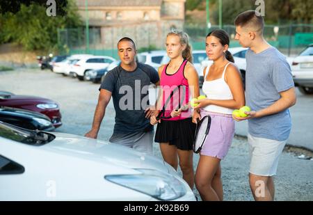 Eine Gruppe von Tennisspielern, die nach dem Spiel auf dem Parkplatz stehen und sich freundlich unterhalten Stockfoto