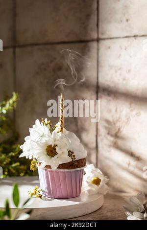 Geburtstagskuchen mit Blumen mit ausgeblasenen Kerzen und Rauchwirbeln auf rosa Fliesen Hintergrund dekoriert. Stillleben Komposition, Jubiläumskonzept Stockfoto