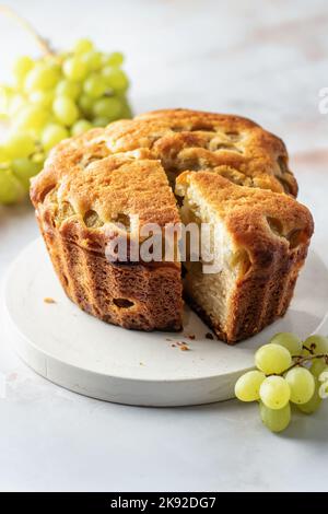 Hausgemachter Kekskuchen oder Kuchen mit weißen frischen Trauben auf weißem Marmorboden. Vertikale Ausrichtung Stockfoto