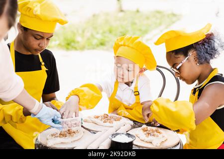 Fröhliche Gesellschaft von multiethnischen Kindern, die Teig kochen. Kinderkochtätigkeit multinationaler Kinder schwarzafrikanischer und kaukasischer Kinder Stockfoto