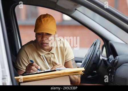 Porträt einer jungen multiethnischen Frau, die einen Lieferwagen fährt und Postformulare ausfüllt Stockfoto