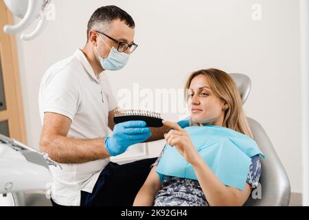 Zahnarzt demonstrieren Zähne Farbtöne Leitfaden für Zahnaufhellung für Frau Patient in der Zahnklinik. Zahnmedizin. Frau, die Veneers oder Implantate ansieht Stockfoto