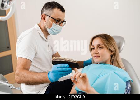 Zahnarzt demonstrieren Zähne Farbtöne Leitfaden für Zahnaufhellung für Frau Patient in der Zahnklinik. Zahnmedizin. Frau, die Veneers oder Implantate ansieht Stockfoto