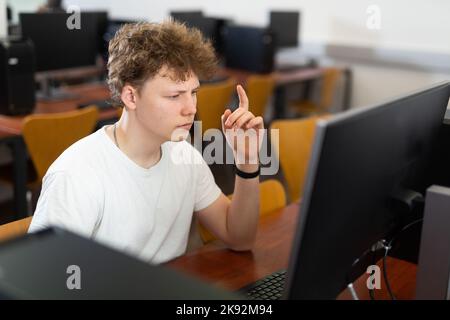 Fokussierter, rätselhafter Teenager, der im Computerlabor studiert Stockfoto