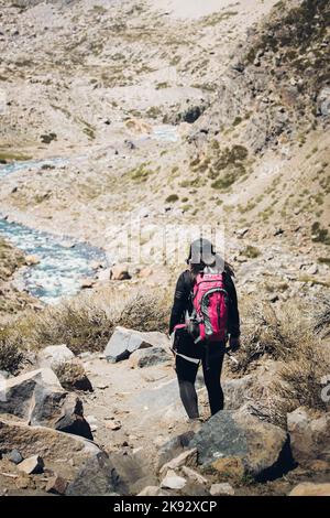 Rückansicht einer Wanderin, die durch einen felsigen Pfad neben einem Bergfluss mit Rucksack geht. Vertikale Aufnahme Stockfoto