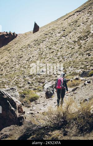 Rückansicht einer Wanderin, die mit einem Rucksack durch einen felsigen Pfad geht. Vertikale Aufnahme Stockfoto