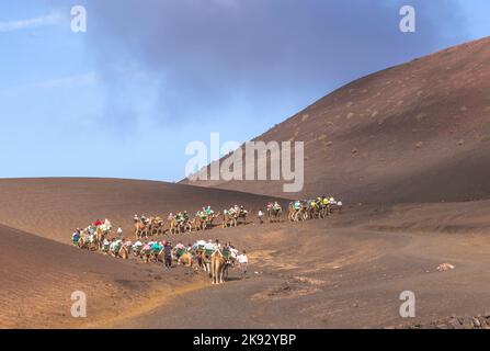 YAIZA, SPANIEN - 15. NOV 2014: Touristen auf einer Kamelsafari im Timanfaya Nationalpark in Yaiza, Spanien. Kamelreiten in Timanfaya ist ein muss für Touristen. Stockfoto