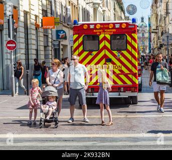 MARSEILLE, FRANKREICH - 10. JULI 2015: Familie wartet am Seitenweg, um die Straße zu überqueren. Ein Krankenwagen mit Reanimation parkt in der Fußgängerzone. Stockfoto