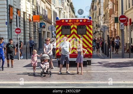 MARSEILLE, FRANKREICH - 10. JULI 2015: Familie wartet am Seitenweg, um die Straße zu überqueren. Ein Krankenwagen mit Reanimation parkt in der Fußgängerzone. Stockfoto