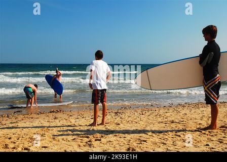 Junge Männer Surfer bereiten sich auf eine Welle zu fangen, tragen ihre Surfbretter zum Meer und einen Sommertag voller Surfen Stockfoto