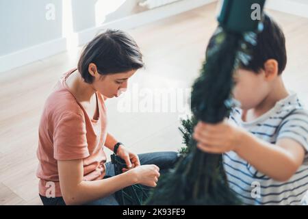 Mutter und Sohn packen den neuen künstlichen Weihnachtsbaum aus, um ihn zu montieren. Glückliche Familie, Kindheit. Menschen leben. Stockfoto