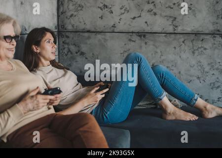 Portrait von überglücklich verschiedenen weiblichen Generationen Familie spielen Videospiele zu Hause, sitzen auf dem Sofa in ihrer Freizeit. Modern für Videospiele Stockfoto