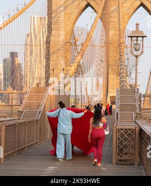 New York City, USA - 18. September 2022: Der sich entwickelnde Zug eines leuchtend roten Kleides während eines Fotoshootings auf der Brooklyn Bridge Stockfoto