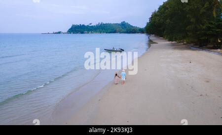 Ein paar Männer und Frauen, die während des Sonnenuntergangs am Strand spazieren, Drone-Luftaufnahme am Klong Prao Beach in Koh Chang, Drone-Blick von oben auf das türkisfarbene Meer. Stockfoto